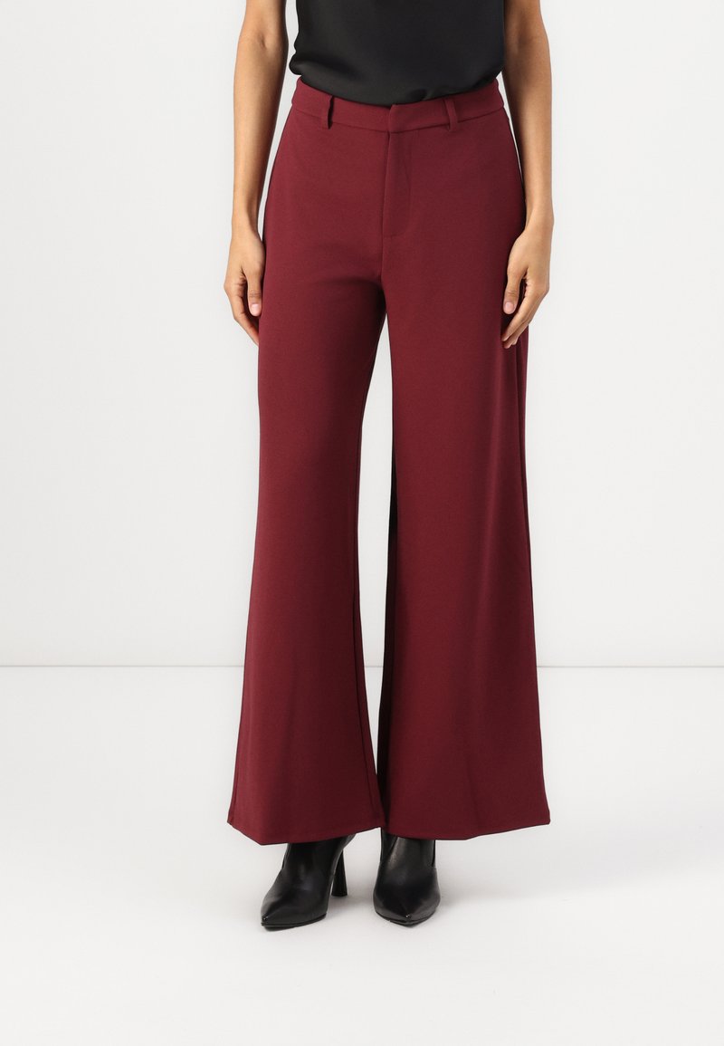 Bordeaux wijde broek met hoge taille, zachte stof en zijsplitten, gecombineerd met zwarte hoge hakken.
