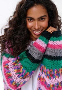 Pletený svetr s výraznými pruhy v růžové, zelené, šedé a barevných akcentů. Pohodlný, strukturovaný materiál s různými vzory.