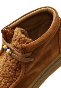 Bruine suède schoen met een zacht, textuurachtig voering en decoratieve kralen in blauw, geel en groen op een bruine veter. Lichtbruine zool.