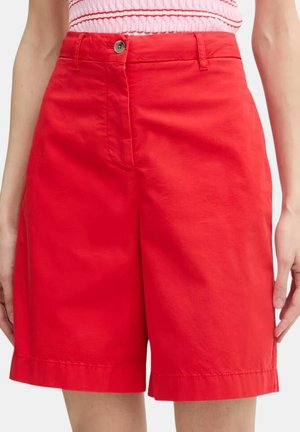 Shorts rossi a vita alta su misura con chiusura a bottone e zip, indossati da una persona con un top senza maniche a righe rosa e rosse.
