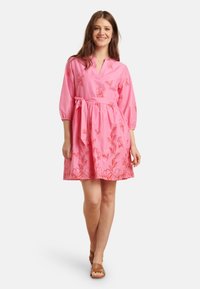 Rosa Kleid mit V-Ausschnitt und dreiviertel Ärmeln, das mit roten Blumenstickereien verziert ist. Ein Taillengürtel rundet das Design ab.