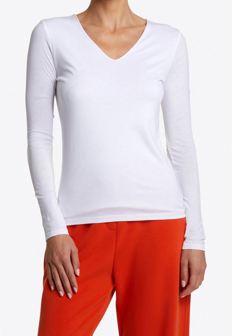 Weißes langärmliges V-Neck-Shirt aus weichem Stoff. Eng anliegendes Design mit minimaler Textur, kombiniert mit leuchtend orangefarbenen Hosen.