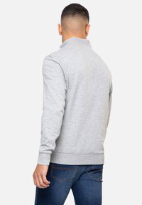 Sweatshirt gris avec un col montant, des manches longues, des poignets et un ourlet côtelés. Fabriqué en tissu doux, avec une texture lisse.