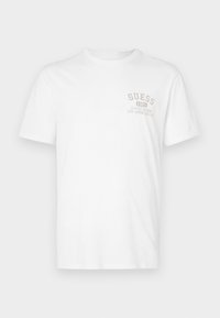 Hvit bomull t-skjorte med korte ermer. Har en beige trykt logo "GUESS 1981" og teksten "KLASSISK DESIGN LOS ANGELES, CA" på brystet.