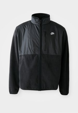 Crna Nike flis jakna s punim patentnim zatvaračem, visokim ovratnikom, zatvorenim džepom na prsima i kontrastnim materijalom na gornjem prednjem dijelu.