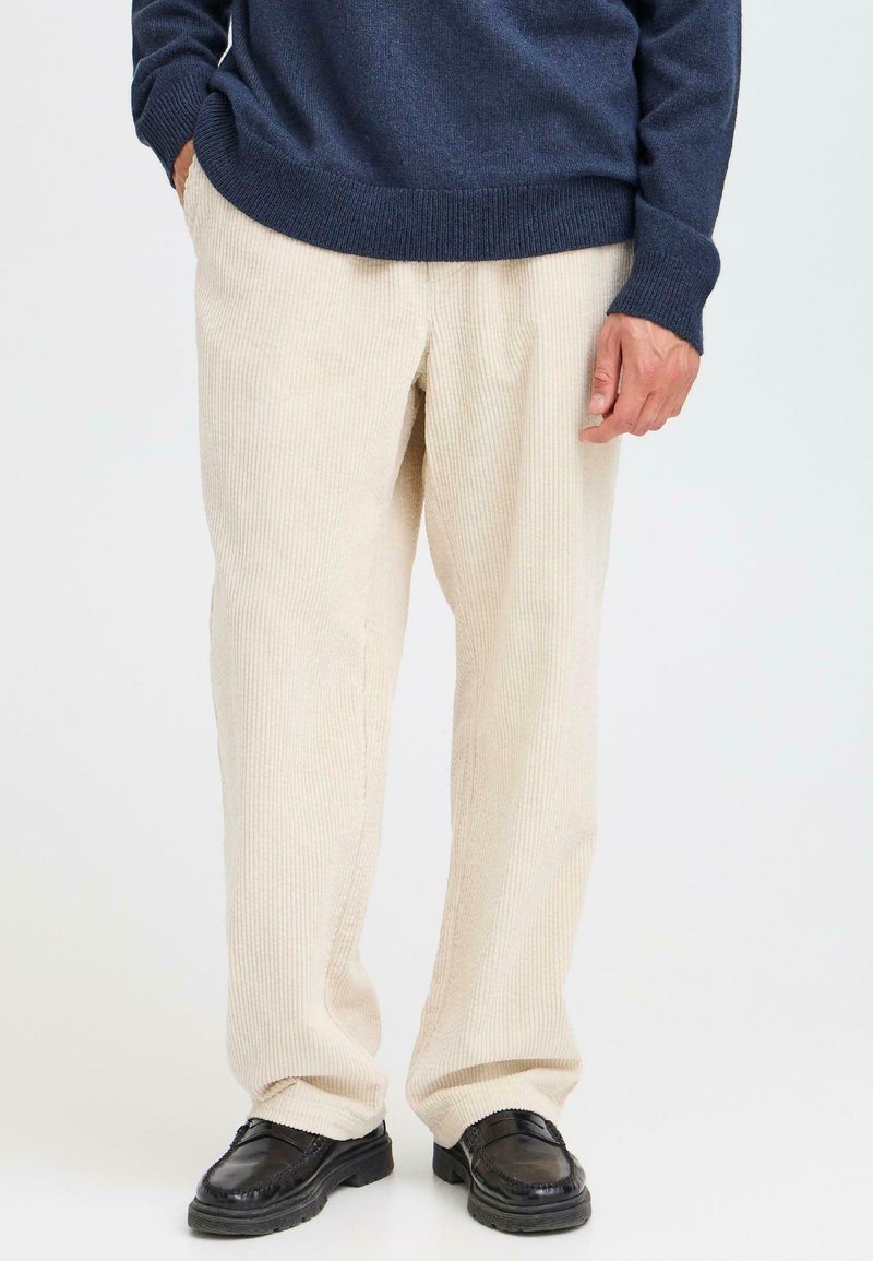 Beige kordfløjspants med ribbet tekstur, sammen med en mørkeblå striktrøje og sorte lædersko. Afslappet pasform og lige ben-design.