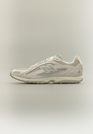 Bézs New Balance sportcipő hálós és velúr panelekből, fűzős, párnázott talppal, oldalnézetben, semleges háttéren.