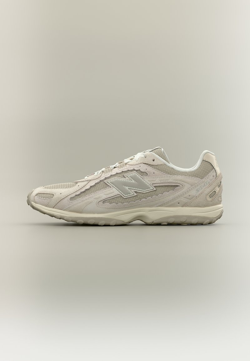 Scarpa da ginnastica New Balance beige con pannelli in mesh e camoscio, chiusura con lacci e suola ammortizzata, mostrata di profilo su sfondo neutro.