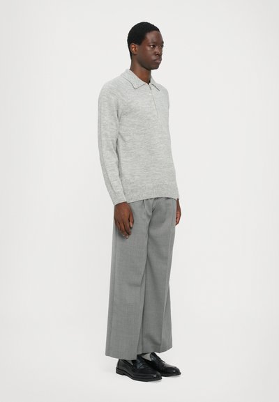 Suéter de punto gris claro con cuello tipo polo y dobladillo acanalado, combinado con pantalones anchos grises y zapatos negros.