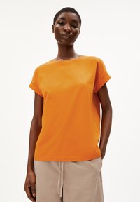 T-shirt en coton orange avec des manches retroussées et un logo brodé sur la poitrine. Il présente une coupe décontractée et une texture lisse.