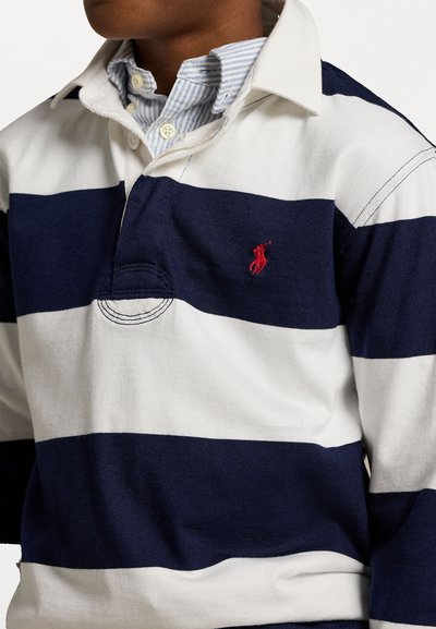 Πολό μπλουζάκι με ναυτικό και λευκές οριζόντιες ρίγες, από βαμβάκι, με δύο κουμπιά στο λαιμό και ένα μικρό κόκκινο έμβλημα στο στήθος.