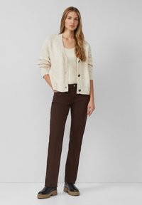Gebreide crèmekleurige cardigan met knoopsluiting, gecombineerd met bruine rechte broeken en zwarte platformlaarzen. Geweven stof en casual ontwerp.