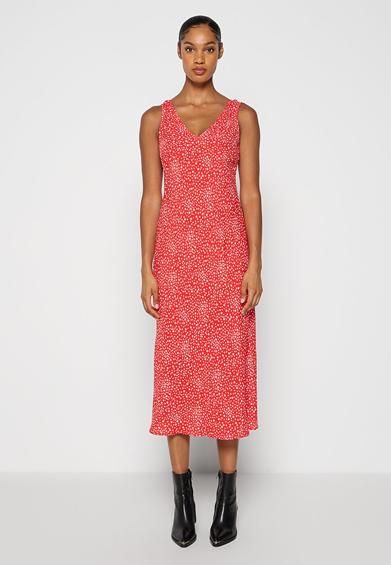 Robe midi fleurie rouge avec un décolleté en V et des bretelles fines. Le tissu a une texture lisse avec des accents de pois blancs. Portée avec des bottines noires.