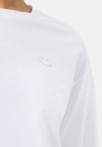 Wit katoenen T-shirt met een klein lichtroze smiley icoon op de borst. Korte mouwen met een ronde hals.