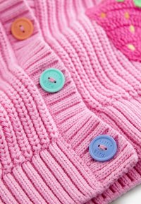 Rózsaszín kötött ruhadarab bordázott textúrával, színes gombokkal: narancs, türkiz és kék, valamint epres mintával a szövetben.