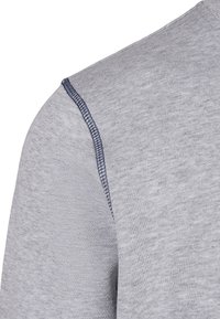 Gros plan d'une chemise en tissu gris clair montrant une couture d'épaule avec une surpiqûre bleu foncé.