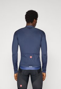 Maillot de cyclisme à manches longues pour homme en tissu bleu marine. Il dispose d'une poche arrière zippée, d'un ourlet élastique et d'un logo réfléchissant. Texture lisse.