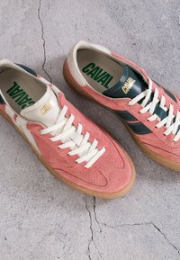 Paire de baskets en daim rose avec lacets blancs, bandes en cuir vert, semelles en gomme et "CAVAL" imprimé sur la languette et les semelles intérieures sur béton fissuré.