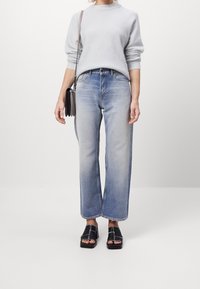 Vybledlé modré široké džíny s vysokým pasem, oblečené s světle šedým svetr a černými sandály s otevřenou špičkou. Oblečení doplňuje malá černá kabelka.