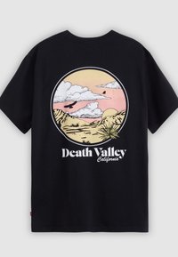 Tricou negru din bumbac cu un grafic circular ce reprezintă un peisaj de deșert cu munți, nori și păsări, etichetat "Death Valley California."