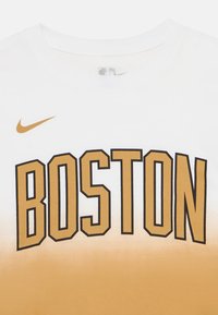 Biała koszulka z gradientem w kolorze złotym i napisem "BOSTON" w pogrubionych czarnych literach. Logo Nike w złotym kolorze na górze po lewej stronie. Materiał z mieszanki bawełny.