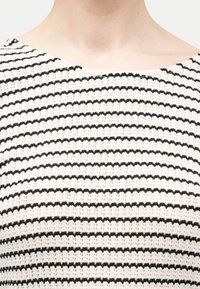 Κοντινό πλάνο ενός ατόμου που φοράει λευκό πλεκτό πουλόβερ με ομοιόμορφα κατανεμημένες λεπτές μαύρες οριζόντιες ρίγες.