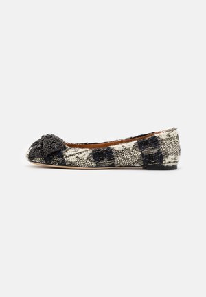 Chaussure plate à carreaux noirs et blancs avec tissu texturé et nœud noir orné de perles sur le bout, vue de profil.