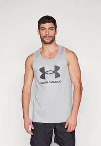 Szürke pamut trikó, amelynek elülső részén egy nagy fekete Under Armour logó található, lekerekített nyakkal és széles karöltőkkel.