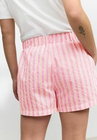 Shorts rayés rose et blancs, taille élastique, poches latérales, tissu léger, texture lisse et longueur mi-cuisse.