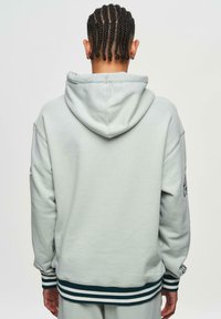 Grå hoodie med en stor huva, ribbade ärmmuddar och randig nederkant. Har en logotyp på vänster ärm och en mjuk, texturerad finish.