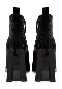 Pari mustia nilkk boots, joissa on kristallikoristeita, vetoketju sivussa ja paksut kiiltävät blokkihäntäiset korkot, nähtynä takana.