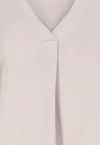 Close-up of light beige fabric with a V-neck seam and subtle texture, showing clean stitching and overlapping material panels.