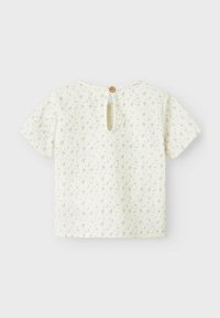 Blusa camicia a maniche corte di colore crema con un piccolo motivo floreale rosa e verde, chiusura con bottoni sul retro e dettaglio a chiave sul collo. Tessuto morbido.