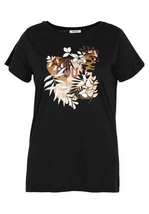 Donna con maglietta nera con motivo floreale marrone e bianco, pantaloni bianchi e sandali arancioni con cinturino alla caviglia, in piedi davanti a uno sfondo bianco.