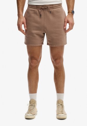 Mand iført brune shorts med snøre, hvide sokker og beige høje sneakers med en hvid t-shirt og et ur på venstre håndled.