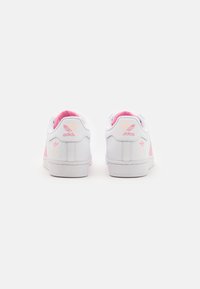 White leather sneakers with pink accents, featuring a padded collar and the Adidas logo on the back. Smooth texture; flat rubber sole.