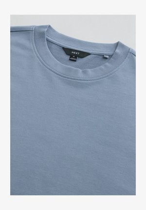 Hellblaues Sweatshirt mit Rundhalsausschnitt, hergestellt aus weicher Baumwolle. Glatte Textur mit geripptem Kragen und subtilen Nähten. Größenetikett sichtbar.