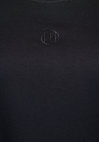 Crna uska majica od pamuka, s teksturiranim, toniranim izvezenim logotipom na sredini. Glatka površina s dizajnom okruglog izreza.