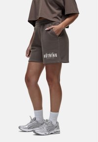 Grijze katoenen shorts met een elastische tailleband en zijzakken, met op het linkerbeen de witte tekst "good for NOTHING ATELIER". Gecombineerd met zilveren sneakers.