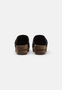 Zoccoli neri aperti sul retro con tacco in legno, caratterizzati da una tomaia in tessuto testurizzato e un design a profilo basso per un uso casual.