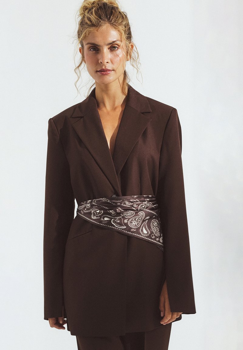 Brauner maßgeschneiderter Blazer mit langen Ärmeln, der mit einem am Bauch gebundenen Paisley-muster Scarf versehen ist. Glattes Material, strukturiertes Design.