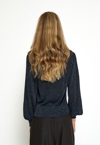 Námornícky modrý trblietavý sveter s dlhými puff rukávmi a priliehavým pásom. Mäkká pletenina s jemným leskom a rebrovaným lemovaním.