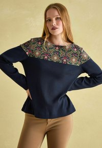 Marineblauer Pullover mit einem floral gemusterten Einsatz in Grün, Rot und Creme. Mit langen Ärmeln und einem Peplum-Saum. Eine glatte Textur.