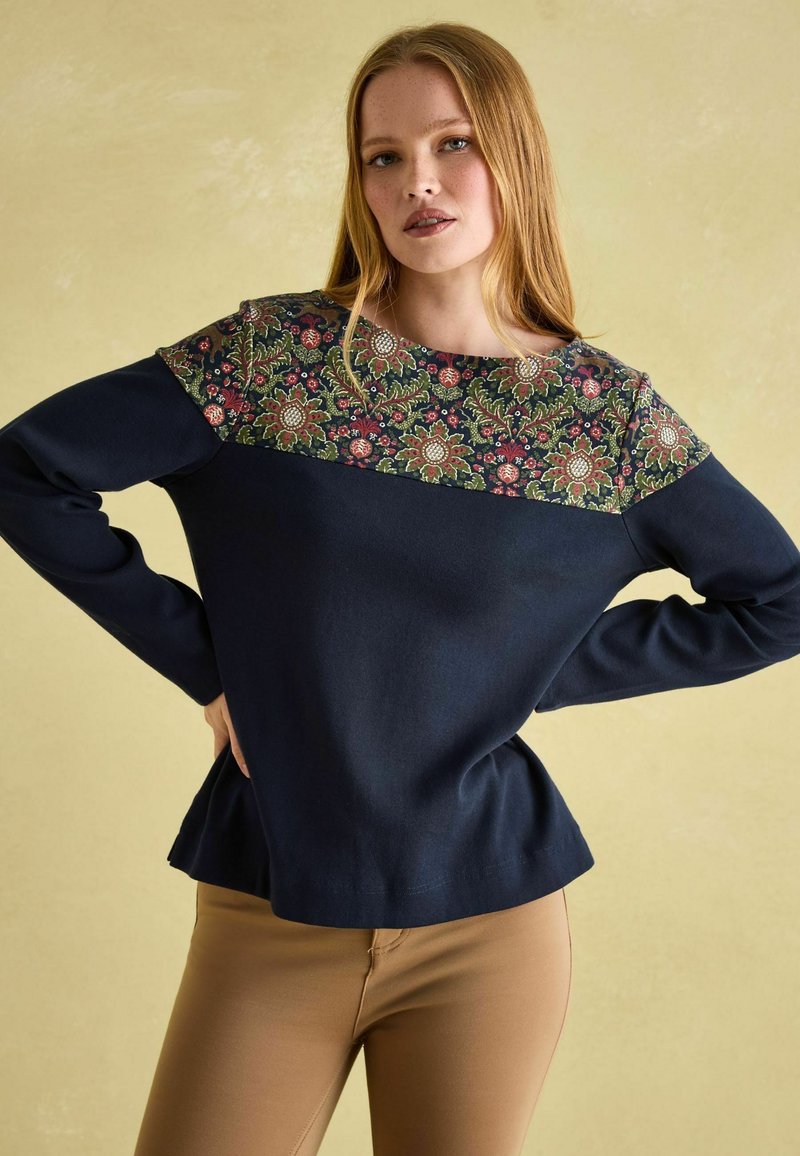 Marineblauer Pullover mit einem floral gemusterten Einsatz in Grün, Rot und Creme. Mit langen Ärmeln und einem Peplum-Saum. Eine glatte Textur.