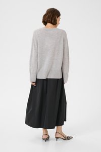 Svetlo sivi pulover z sproščenim krojem, dolgimi rokavi in ribanim robom, v kombinaciji s črno, lepršavo, dolžino do gležnjev krilom in patterned čevlji.