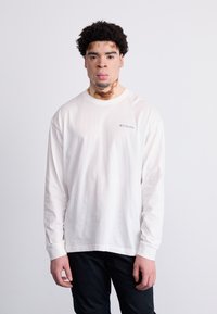 Witte blouse met lange mouwen en ronde halslijn, met opgerolde mouwen en een klein blauw Columbia-logo op de borst.