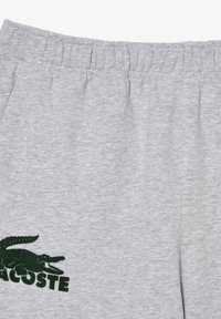 Grå sweatpants laget av myk bomull, med elastisk midje og en grønn brodert krokodillelogo på venstre lår.