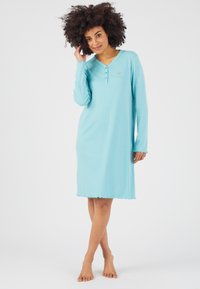 Nuisette en coton bleu clair avec des manches longues, un décolleté en v et une patte de boutonnage à trois boutons. L'ourlet festonné ajoute une touche délicate.