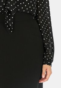 Czarna bluzka w białe kropki, z długimi rękawami i związanym kołnierzykiem, połączona z czarną spódnicą o wysokim stanie z kieszeniami bocznymi.