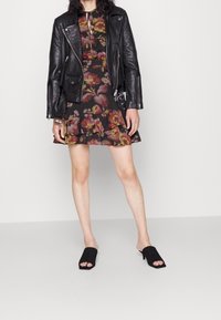 Musta nahkainen moottoripyörätakki, kukkakuosiset mekot röyhelöillä ja mustat avointopohjaiset kengät. Korostaa yksityiskohtaisia kukka- ja lehväkuvioita.